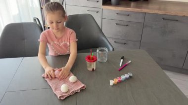 Çocuk boyamadan önce havluyla beyaz yumurta düzenliyor. Paskalya geleneklerinin ilk adımlarını ve odaklanmış hazırlıkları gösteriyor..