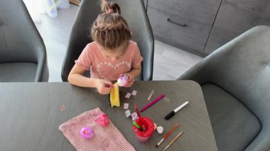 Küçük kız evde otururken Paskalya yumurtalarını renkli çıkartmalarla süslüyor. Yaratıcı Paskalya aktivitesi, basit yumurta süsleme tekniği ve kapalı alanda neşeli tatil hazırlığı.