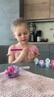 Mutfakta yumurtaları süslerken gülümseyen genç bir kız. Paskalya geleneklerine neşeli bir katılım ve aile bağları. Mevsimsel yaratıcılık, evde festival geleneği ruhu.