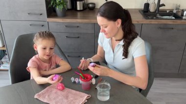 Anne ve kızı evde otururken Paskalya yumurtalarını renkli çıkartmalarla süslüyorlar. Aile Paskalya Sanatları etkinliği, paylaşılan yaratıcılık ve eğlenceli tatil hazırlıkları..
