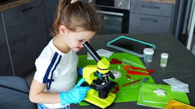 Kristal yapısını mikroskopla inceleyen genç bir kız. Büyüyen kristallerle yapılan deney sırasında. Erken STEM eğitimi ve merakı, bilimsel keşifleri yurtiçinde yürütüyor