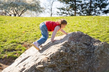 Şehir parkında dekoratif taşların üzerine atlayan küçük bir kız. Aktif bahar eğlencesi ve açık hava çocukluk hayatı.