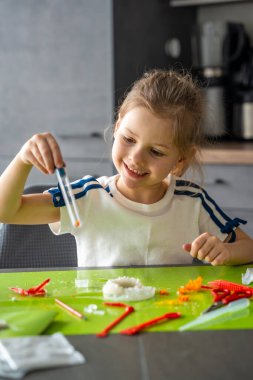 Küçük bir kristalle test tüpü tutan ve dikkatlice incelenen genç bir kız laboratuvar masasında sonuç veriyor. Bilimsel gözlem, kristal büyüme deneyi yoluyla pratik BTMM öğrenmesi