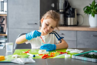 Evde kristal yetiştirme deneyi sırasında kaşığı bardakta ölçerek kimyasal çözeltiyi karıştıran genç bir kız. Kimya pratiği ve uygulamalı laboratuvar faaliyetleri yoluyla erken STEM eğitimi