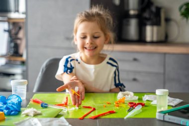 Evde bilim masasında farklı şekillerde renkli kristaller tutan çocuk eli. Kristal büyüyen deney sonuçları ve pratik öğrenme yoluyla BTMM keşfi elleri