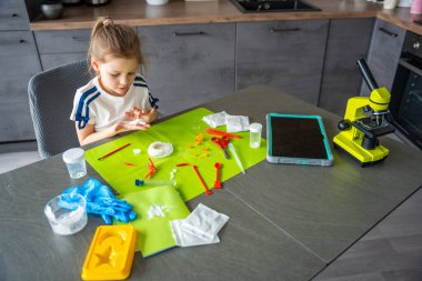 Yıldız şeklindeki kristali tutan genç bir kız evdeki laboratuvar masasında yüzeyini ve dokusunu dikkatlice inceliyor. Kristal yetiştirme deneyi ve bilimsel keşifler üzerine erken STEM eğitimi