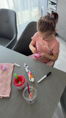 Mutfakta yumurtaları süslerken gülümseyen genç bir kız. Paskalya geleneklerine neşeli bir katılım ve aile bağları. Mevsimsel yaratıcılık, evde festival geleneği ruhu.