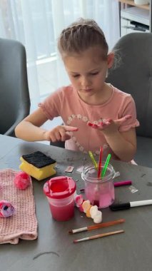 Küçük kız evde otururken Paskalya yumurtalarını renkli çıkartmalarla süslüyor. Yaratıcı Paskalya aktivitesi, basit yumurta süsleme tekniği ve kapalı alanda neşeli tatil hazırlığı.