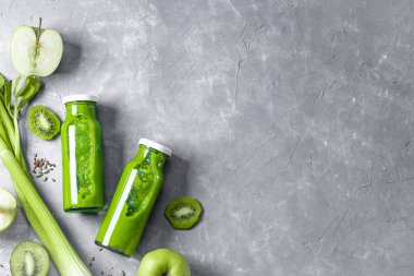  Gri arka plan manzaralı, kivili, kerevizli ve yeşil elmalı iki smoothie şişesi, mesaj için boş yer. Yüksek kalite fotoğraf