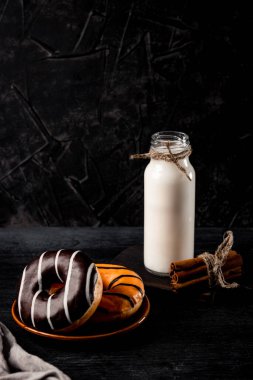  Tabakta tatlı çörekler ve siyah arka planda bir şişe süt, dikey fotoğraf, mesaj için boş yer. Yüksek kalite fotoğraf