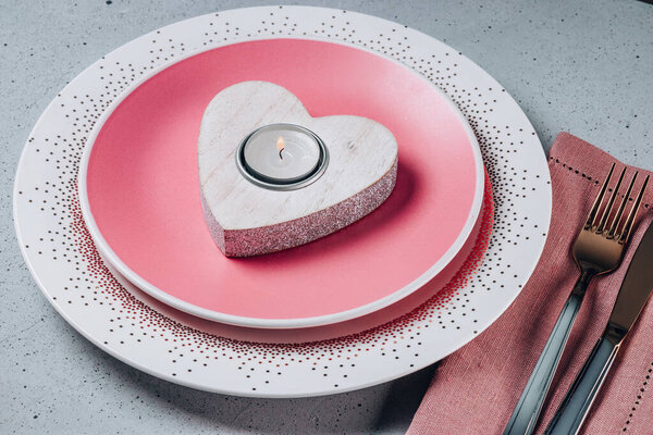  Empty pink plate, cutlery and heart shaped candle on the table. Saint Valentines day table setting