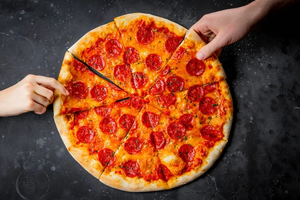 Mani prendere pezzi di pizza classica italiana salame piccante su sfondo nero, vista dall'alto — Foto Stock