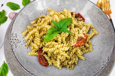  Pesto soslu İtalyan makarnası ve beyaz ahşap bir masada kurutulmuş domates.