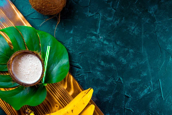 Coquetel de banana de coco em casca de coco na folha de monsterra, foto com espaço livre para texto — Fotografia de Stock