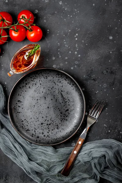 Placa vacía, tenedor, tomates y aceite en bote de salsa sobre fondo negro vista superior — Foto de Stock