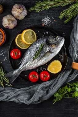 Çiğ dorado balığı ve baharatlar, siyah arka planda tavada pişirmek için, en üstteki dikey fotoğrafta.