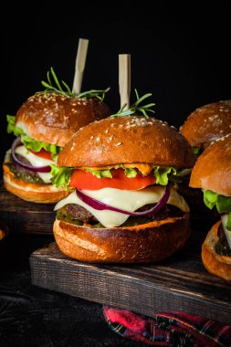 Siyah arka planda peynirli birkaç ev yapımı burger, dikey fotoğraf.