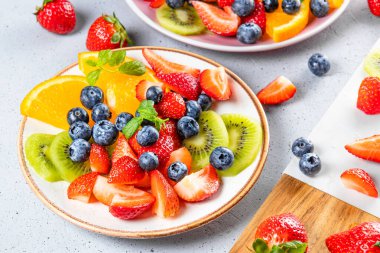 Çeşitli meyve ve meyvelerden oluşan taze yaz salatası. Kivi, portakal, çilek ve böğürtlen. Masada naneyle süslenmiş bir tabakta.