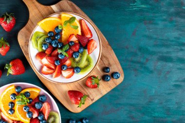 Çeşitli meyve ve meyvelerden oluşan taze yaz salatası. Kivi, portakal, çilek ve böğürtlen mavi ahşap arka plan manzaralı nane ile dekore edilmiş bir tabak, metin için boşluk kopyala