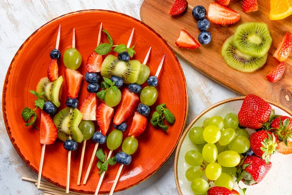 Frutas frescas de verão em paus. Morangos, uvas, mirtilos e kiwi em uma apresentação original. Lanche leve de um banquete de verão — Fotografia de Stock