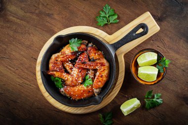  Susam tohumlu fırında tavuk kanadı, maydanoz ve limon siyah bir tavada ve ahşap arka plan manzaralı.