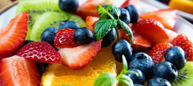 Çeşitli meyve ve meyvelerden oluşan taze yaz salatası. Web sitesi için naneyle süslenmiş bir tabakta kivi, portakal, çilek ve yaban mersini.