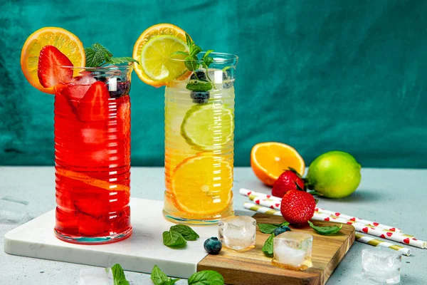 Twee glazen verfrissende zomerlimonade met ijs. Cocktail met aardbei en citroen en cocktail met citroen en limoen op de groene achtergrond — Stockfoto