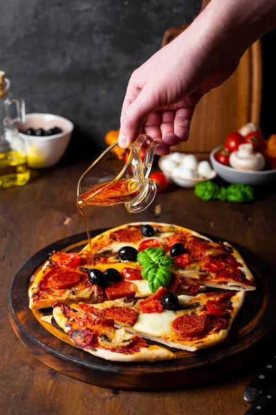 Lo chef versa olio d'oliva sulla pizza italiana fatta in casa con mozzarella, salsicce al peperoncino, olive e basilico, foto verticale — Foto Stock
