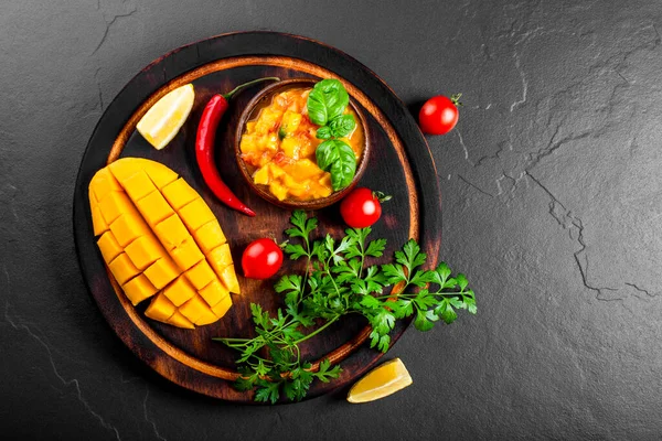 Salsa mexicana picante con mango, chile, tomates y albahaca en un tazón de madera en el fondo negro vista superior — Foto de Stock