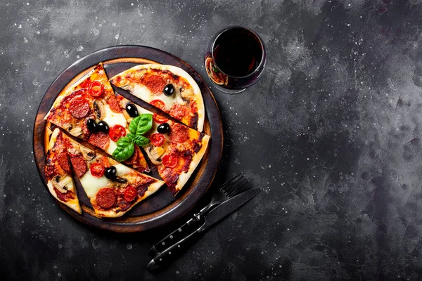 Pizza italiana fatta in casa con mozzarella, salsicce al peperoncino, olive e basilico e un bicchiere di vino rosso su sfondo grigio scuro top view copy space for text — Foto Stock