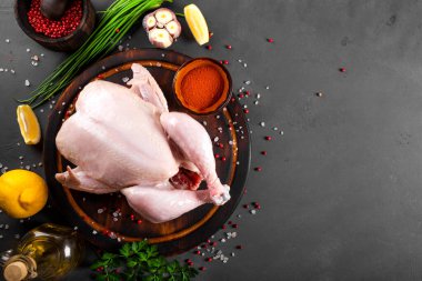 Ahşap kesim tahtasının üzerinde çiğ tavuk ve onu pişirmek için baharatlar, yazı için bedava alan. Koyu gri arkaplan