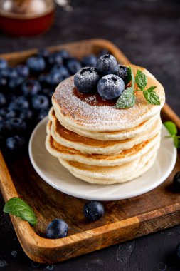 Masanın üzerinde yaban mersinli ev yapımı krep ve pudra şekeri var.