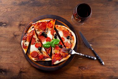 Ev yapımı İtalyan pizzası mozzarella, sucuklu sosis, zeytin ve fesleğen ve masanın üstünde bir bardak kırmızı şarap.