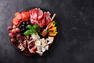  A set of appetizers for wine, jamon, pepperoni, cheese, grapes, peach and olives on a wooden board top view. Snack board on dark gray background, free space for text