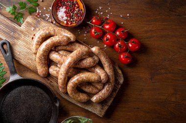 Raw meat sausages from beef and minced pork on wooden cutting board and products for cooking it top view