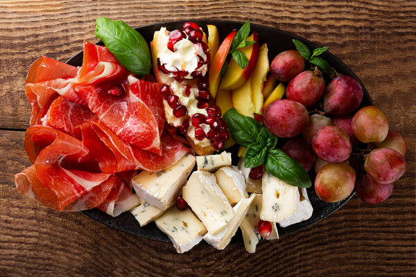  A set of appetizers for wine, jamon, pepperoni, cheese, grapes, peach on a plate top view. Snack board on wooden background, close up