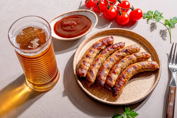 Embutidos de carne picada a la parrilla y cerdo con salsa barbacoa en un plato y un vaso de cerveza en la mesa, foto con luz solar y sombras — Foto de Stock