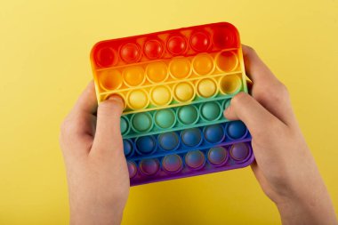 Çocukların eli yeni moda bir silikon oyuncak oynuyor. Anti-stres, sarı arka planda, üst tarafta.