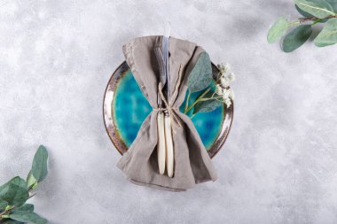  Düğün masası konsepti. Tabak, keten peçetedeki çatal bıçak takımı ve açık gri arka plandaki çiçekler, üst manzara.