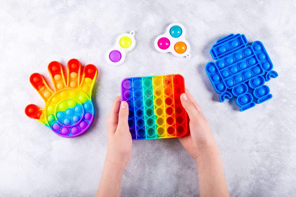 Childrens hand is playing a new trendy silicone toy antistress pop it, next to other toys pop it and simple dimple. Top view