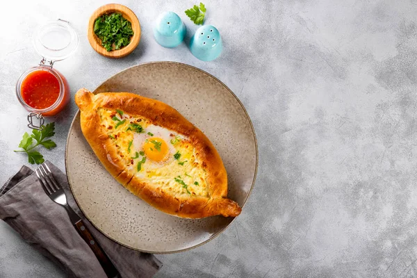 Un plat traditionnel de la cuisine géorgienne, Adjarian khachapuri avec fromage et oeuf et sauce tomate épicée adjika sur le fond gris clair vue du dessus copier l'espace pour le texte — Photo