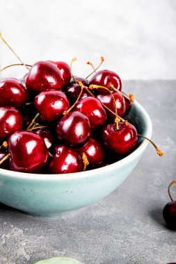 Açık gri arka planda olgun bir kiraz, masanın üstünde yaz meyveleri, dikey fotoğraf.