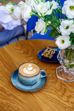 Kafede bir fincan kapuçino kahve ve çiçekler, dikey fotoğraf.