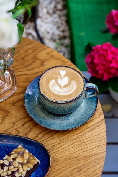 Eine Tasse Cappuccino-Kaffee und Blumen auf einem Tisch in einem Café, vertikales Foto — Stockfoto