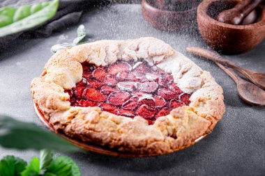 Pudra şekeri ev yapımı turtanın üzerine dökülür. Masada çilek, meyveli yaz çörekleri.