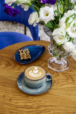 Kafede bir fincan kapuçino kahve ve çiçekler, dikey fotoğraf.