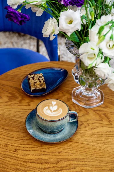 Kafede bir fincan kapuçino kahve ve çiçekler, dikey fotoğraf.