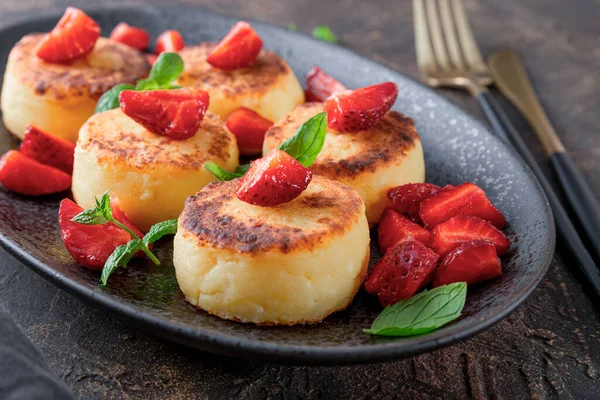  Çilekli süzme peynir krepleri ve siyah masada siyah bir tabakta naneli şekerler.