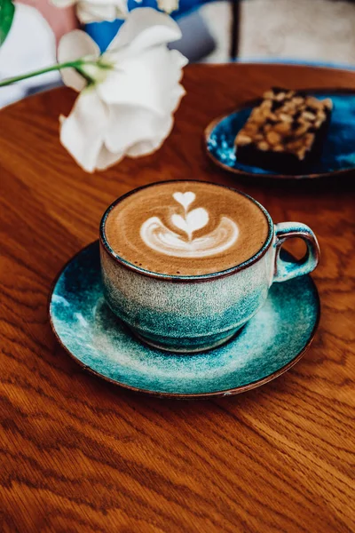 Eine Tasse Cappuccino-Kaffee und Blumen auf einem Tisch in einem Café, vertikales Foto — Stockfoto