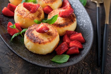  Çilekli süzme peynir krepleri ve siyah masada siyah bir tabakta naneli şekerler.